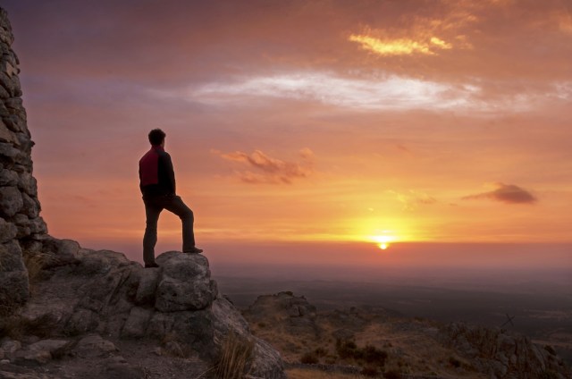 Man on top of a mountain standing contemplates the dawn